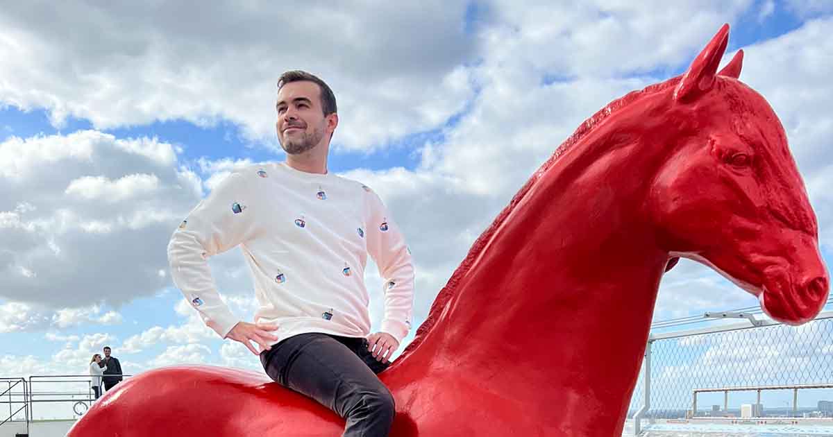 Jake sitting on a large red horse statue, looking off into the distance